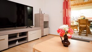 A living room with a flat-screen TV, wooden furniture, a vase with flowers, and a view of the outside. - House Rajka I (Vodice)