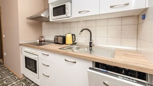 A compact kitchen with white cabinets, a microwave, a toaster, a kettle, and a dishwasher. - House Rajka I (Vodice)