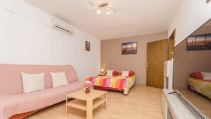A modern room with a pink sofa, a wooden table, a bed with a colorful striped bedspread, and a wooden door. - House Rajka I (Vodice)