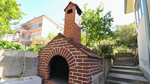 A brick-built outdoor oven, a concrete staircase, and a building with balconies in the background. - Apartment Katica (Trogir)