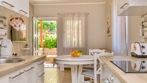 Una cocina moderna con armarios blancos, una mesa redonda con sillas, un frutero y una cafetera.