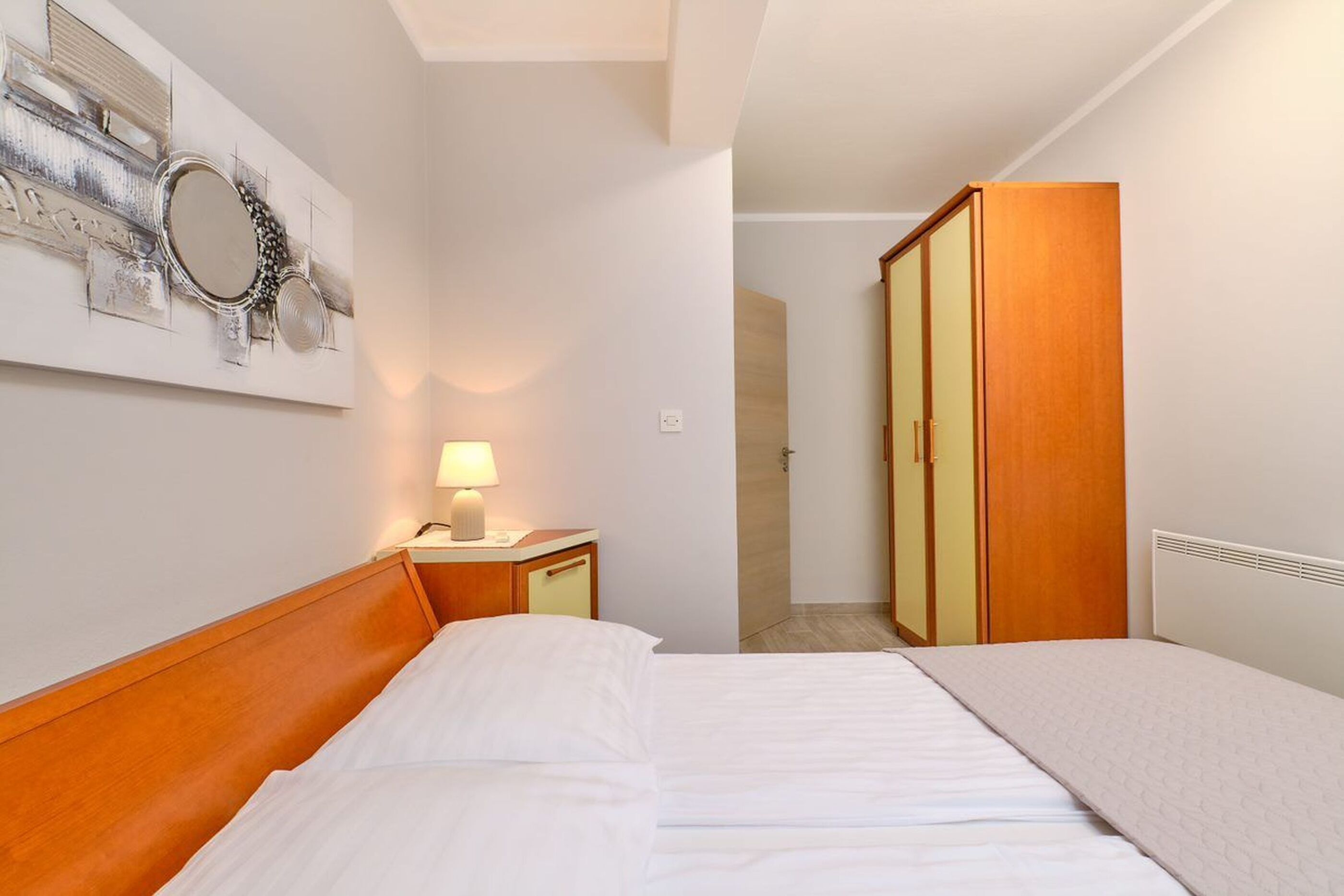 Ein Hotelzimmer mit einem Bett, einem Nachttisch mit Lampe, einem Schrank und einem an der Wand befestigten Spiegel.