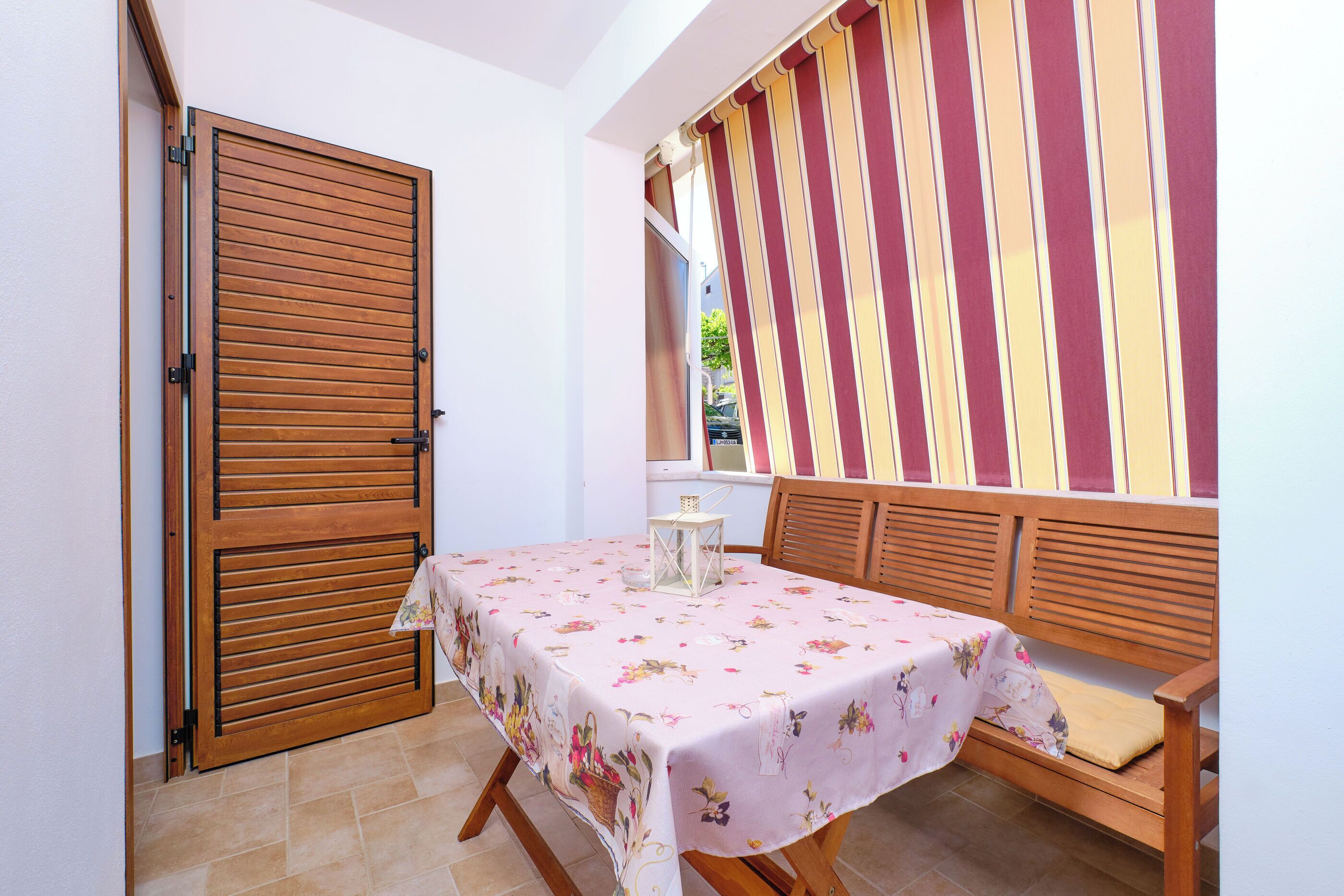 A dining area with a table covered in a floral tablecloth, a bench, and a striped wall.