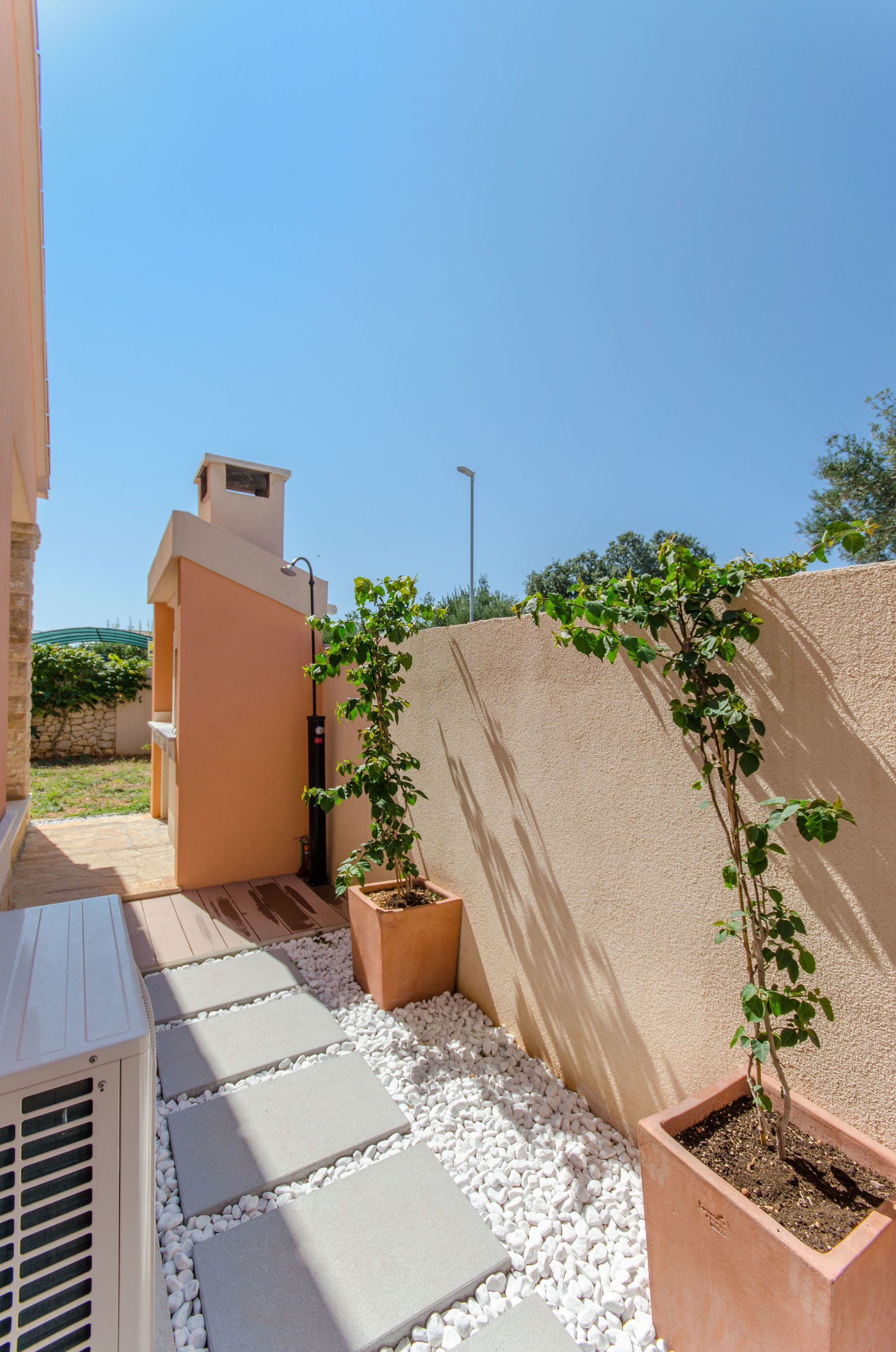 A courtyard with a beige wall, a small tree, and a white air conditioning unit.