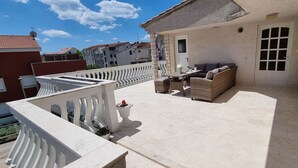 A balcony with outdoor furniture, a white railing, and a view of neighboring buildings. - Apartment Heaven (Strozanac)