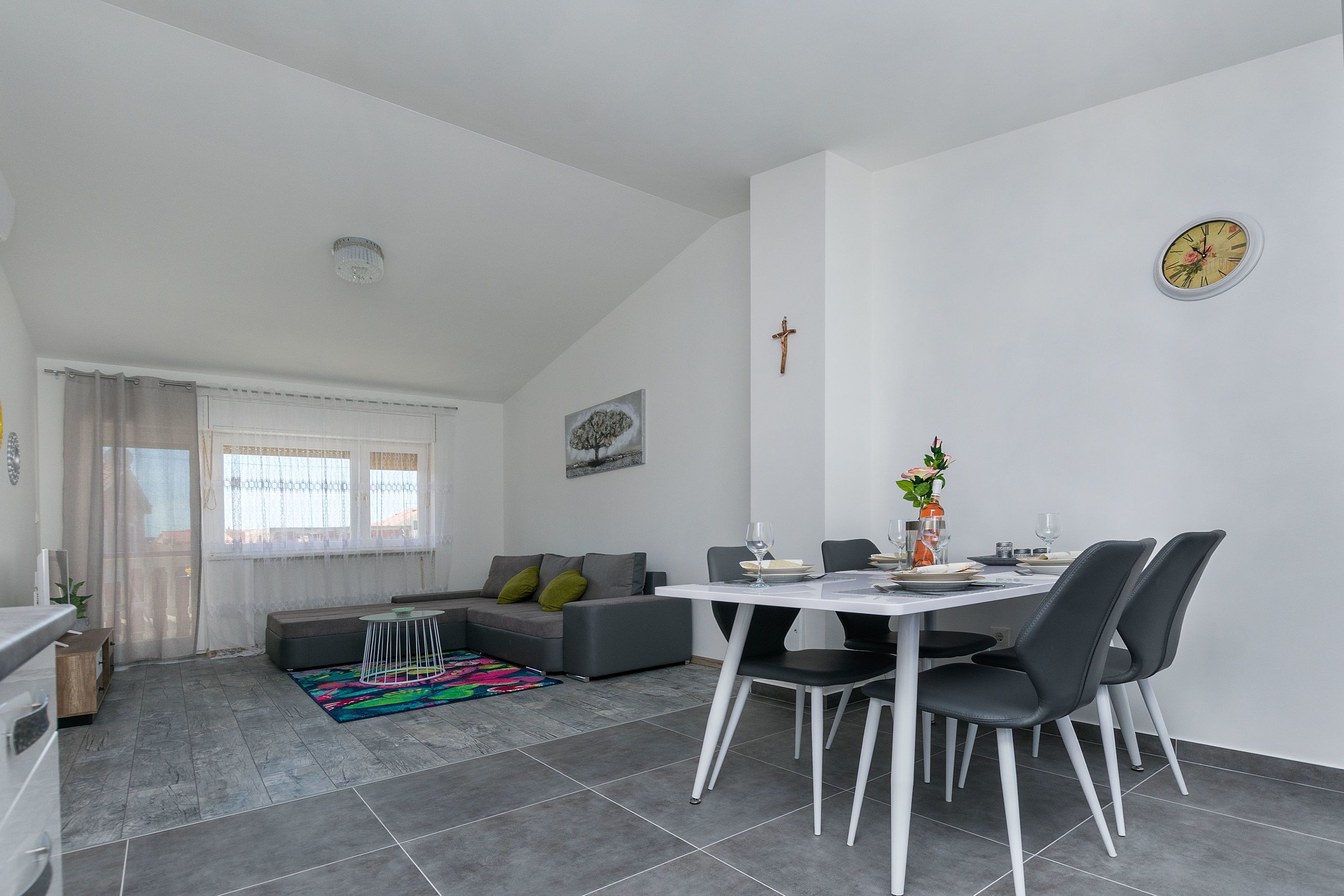 A modern living room with a dining area, grey sofa, and a white table with chairs.