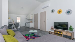 A modern living room with a grey sofa, a small round coffee table, and a TV on a wooden stand. - Apartment Heaven (Strozanac)
