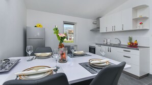 A modern kitchen with white cabinetry, a built-in oven, and a window with a city view. - Apartment Heaven (Strozanac)