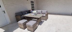 An outdoor patio with wicker furniture, including a sofa and ottomans, and a table with a vase of flowers. - Apartment Heaven (Podstrana)