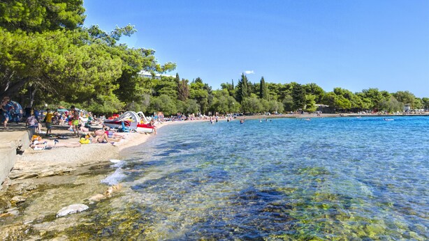 Une plage à l’eau claire, où l’on peut voir des gens se prélasser au soleil, et une rive sablonneuse.