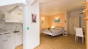 Une petite pièce comprenant un coin cuisine, un lit, une table de chevet et une chaise.