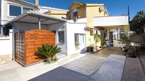 Une maison à deux étages avec un patio couvert, une porte en bois et des plantes en pot.