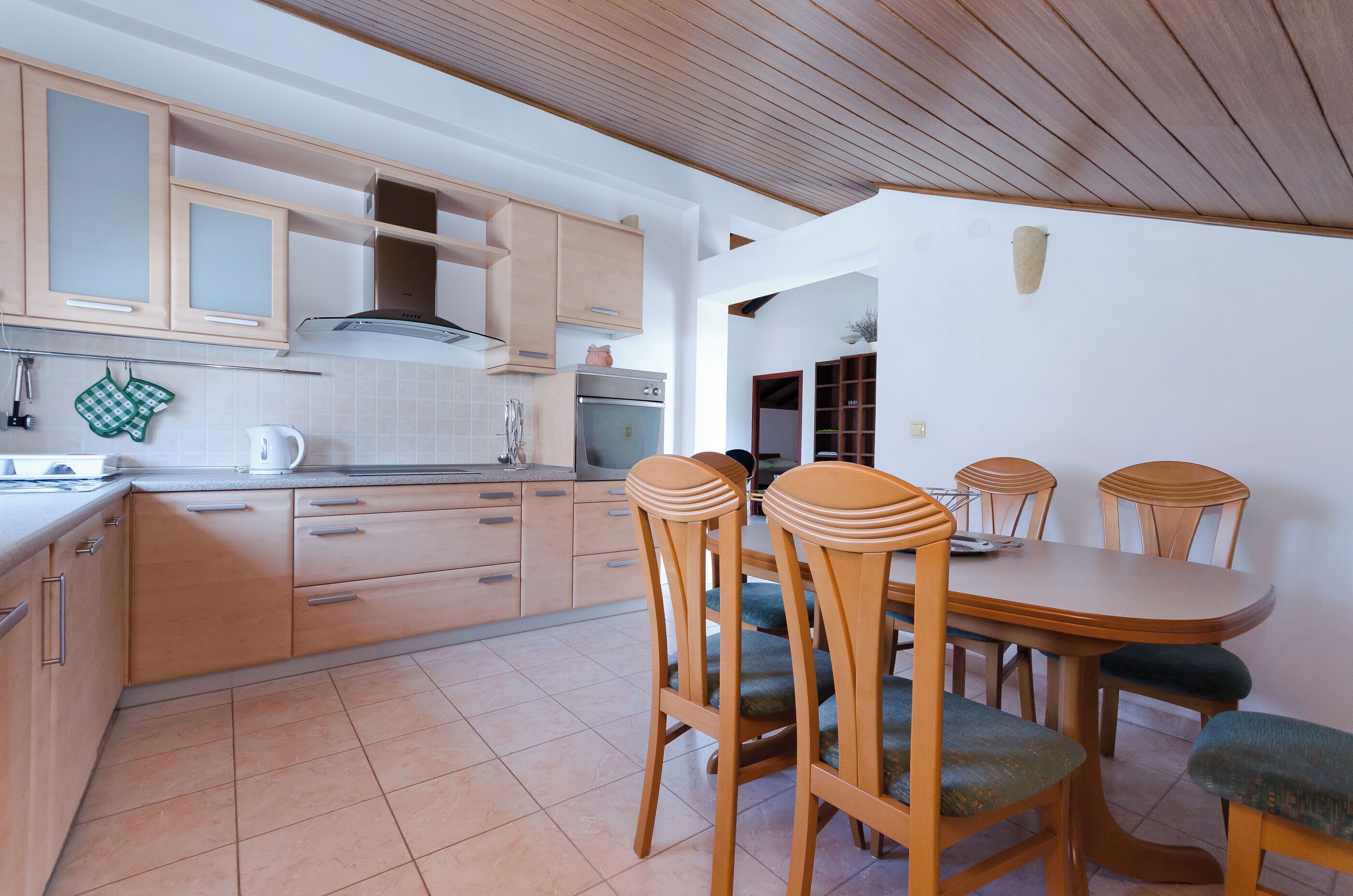 Una cucina con mobili in legno, un tavolo da pranzo con sedie e un pavimento piastrellato.