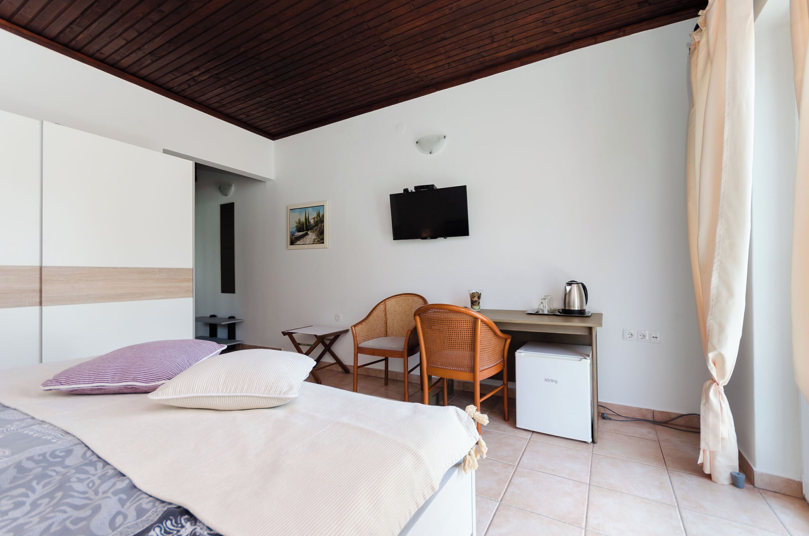 A bedroom with a bed, a desk, a chair, a small refrigerator, and a television on the wall.
