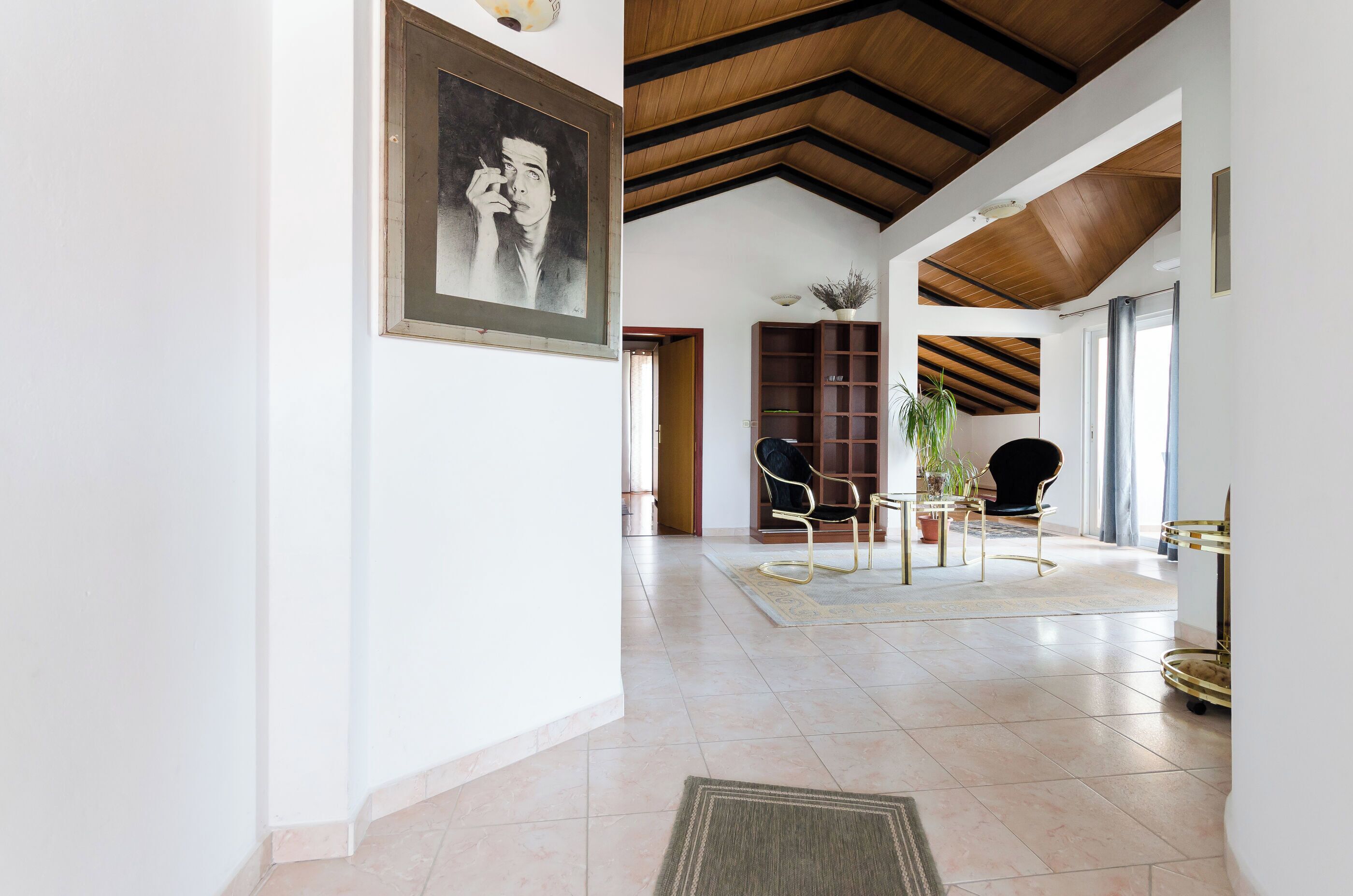 A spacious living area with a high ceiling, tiled floor, and a large painting on the wall.
