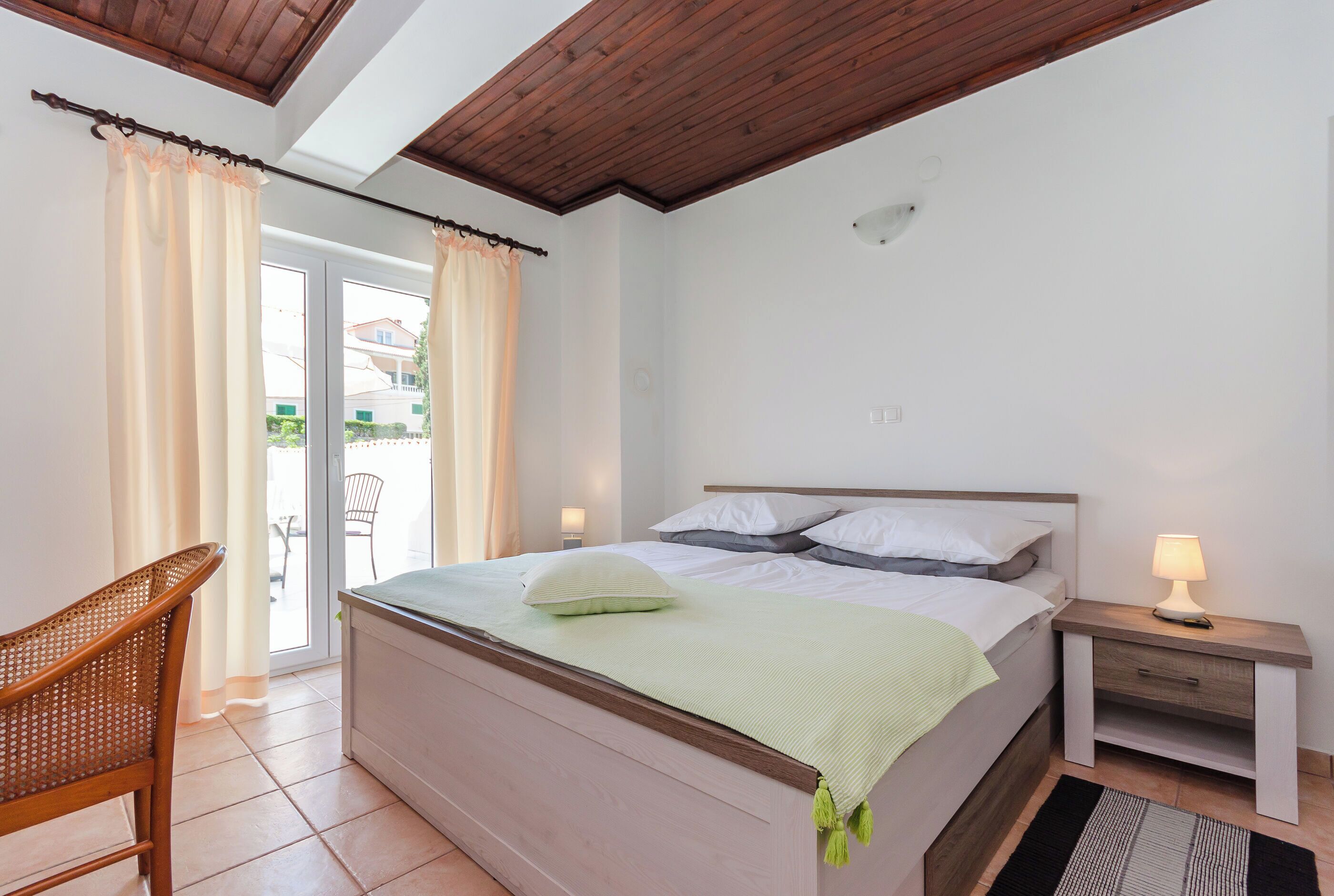 A bedroom with a bed, bedside table, chair, and a view through a glass door.