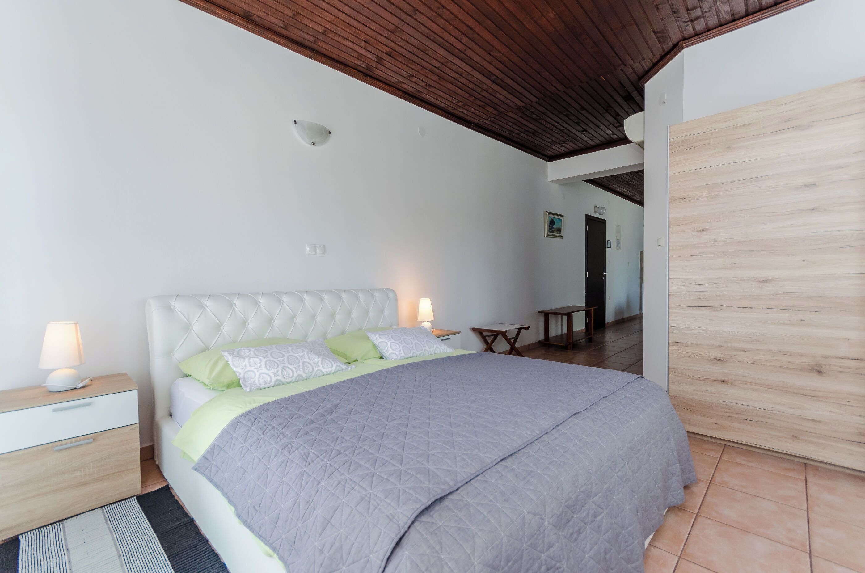 Una camera da letto con un letto grande, un soffitto in legno, un comodino con una lampada e un armadio in legno.
