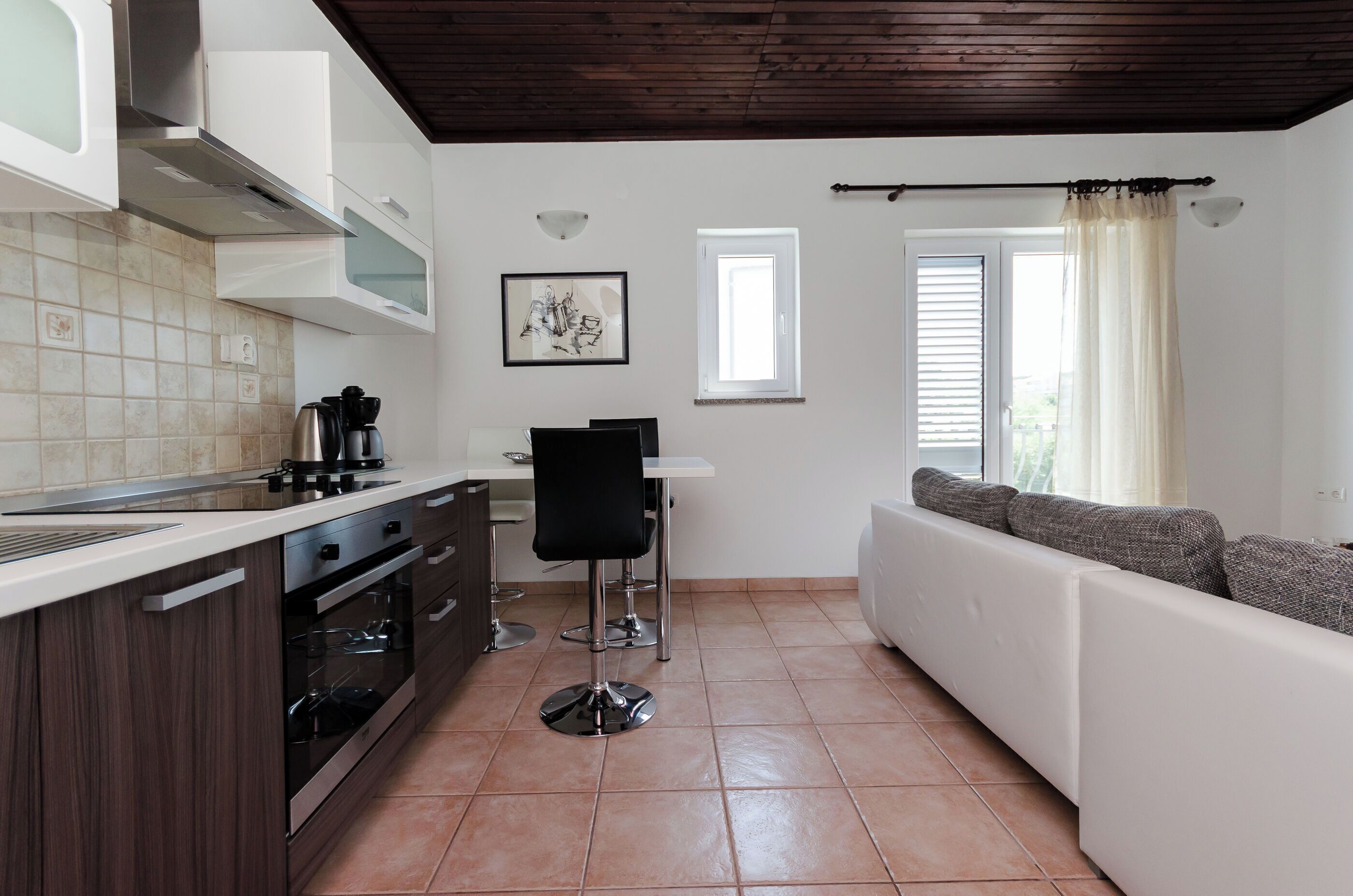 A modern kitchen with a dining area, a sofa, and a window with blinds.