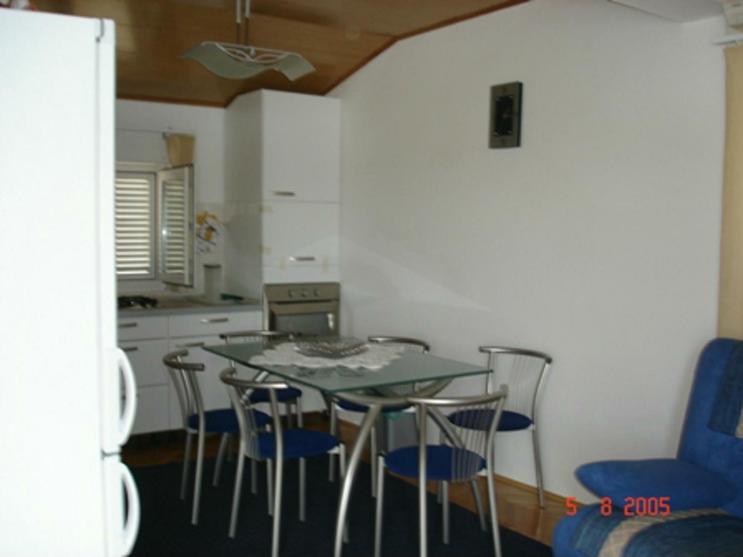 A compact kitchen with white cabinets, a stove, and a dining area with a glass table and metal chairs.