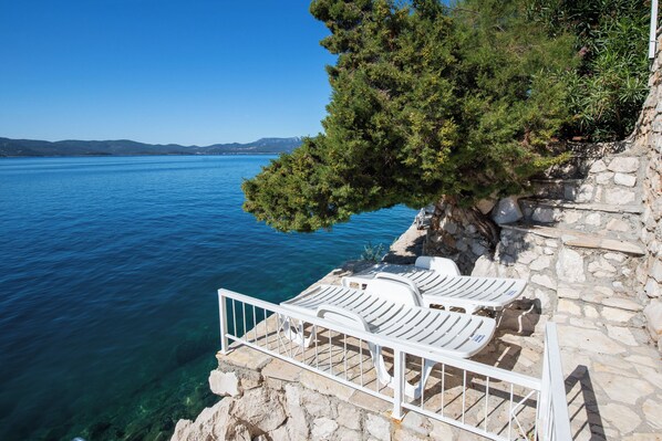 A stone terrace with white lounge chairs overlooking a clear blue sea. - Apartments Vesna (Komarna)