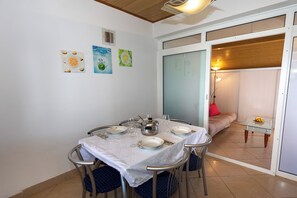 A dining area with a table set for four, chairs, a wall clock, and a sliding glass door leading to a living space. - Apartments Vesna (Komarna)