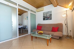 A living room with a glass coffee table, a sofa with red cushions, a dining area with a table and chairs, and a painting on the wall. - Apartments Vesna (Komarna)