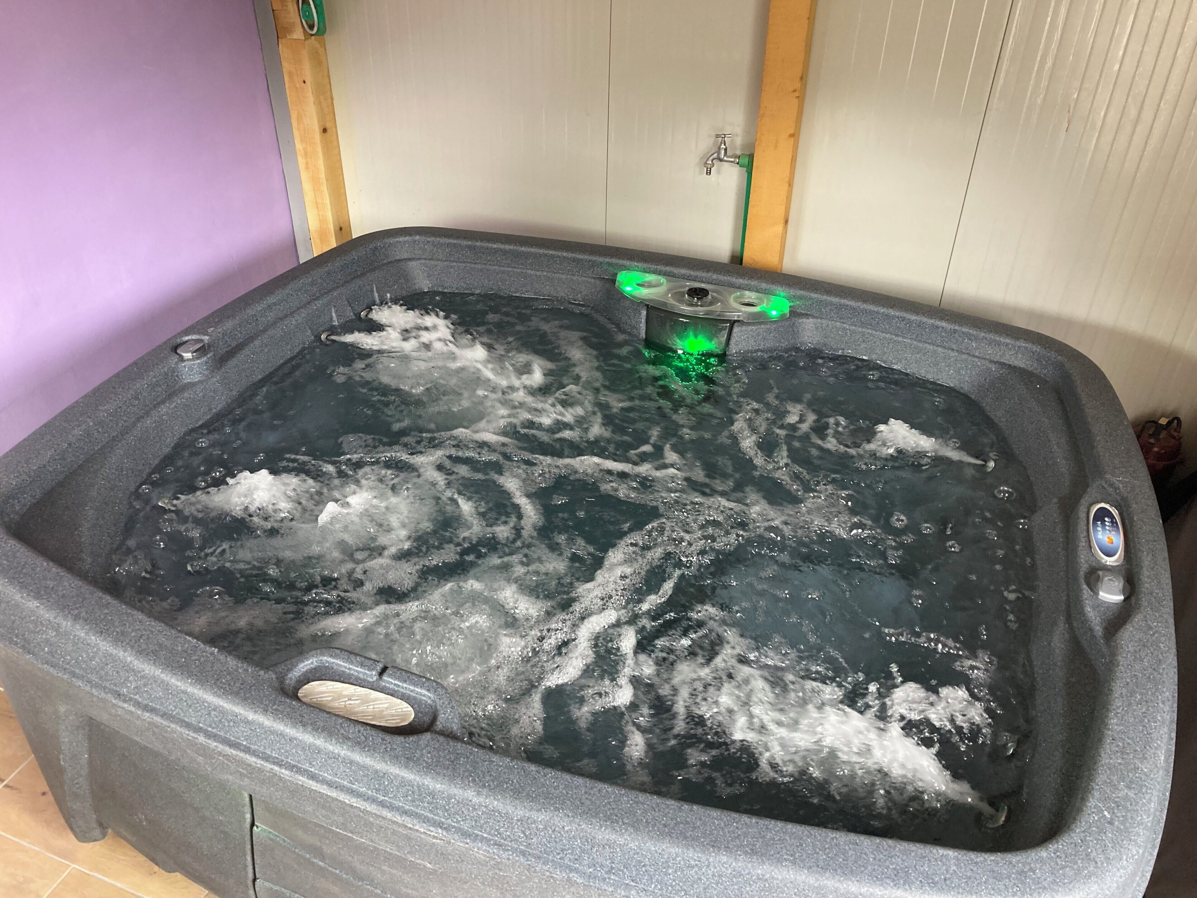Una bañera de hidromasaje con luz verde, un panel de control y un grifo.