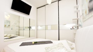 A modern bedroom with a large bed, a flat-screen TV mounted on the wall, and a large mirror reflecting the room. - Apartment Anja (Jesenice)
