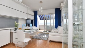 A modern kitchen with white cabinets, a dining area with a glass table, and a sofa. - Apartment Anja (Jesenice)
