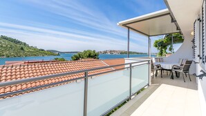 Un balcon doté d’une balustrade en verre, donnant sur une zone côtière avec des tuiles en terre cuite et comprenant une table avec des chaises.