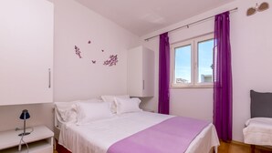 Une chambre à coucher avec un lit, une table de chevet, une chaise, une fenêtre avec des rideaux violets et des éléments de décoration murale.
