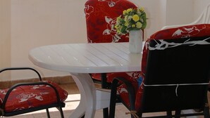 A balcony with a white table and chairs, a vase with flowers, and a view of the sea. - Apartments and Room Janja (Primosten)