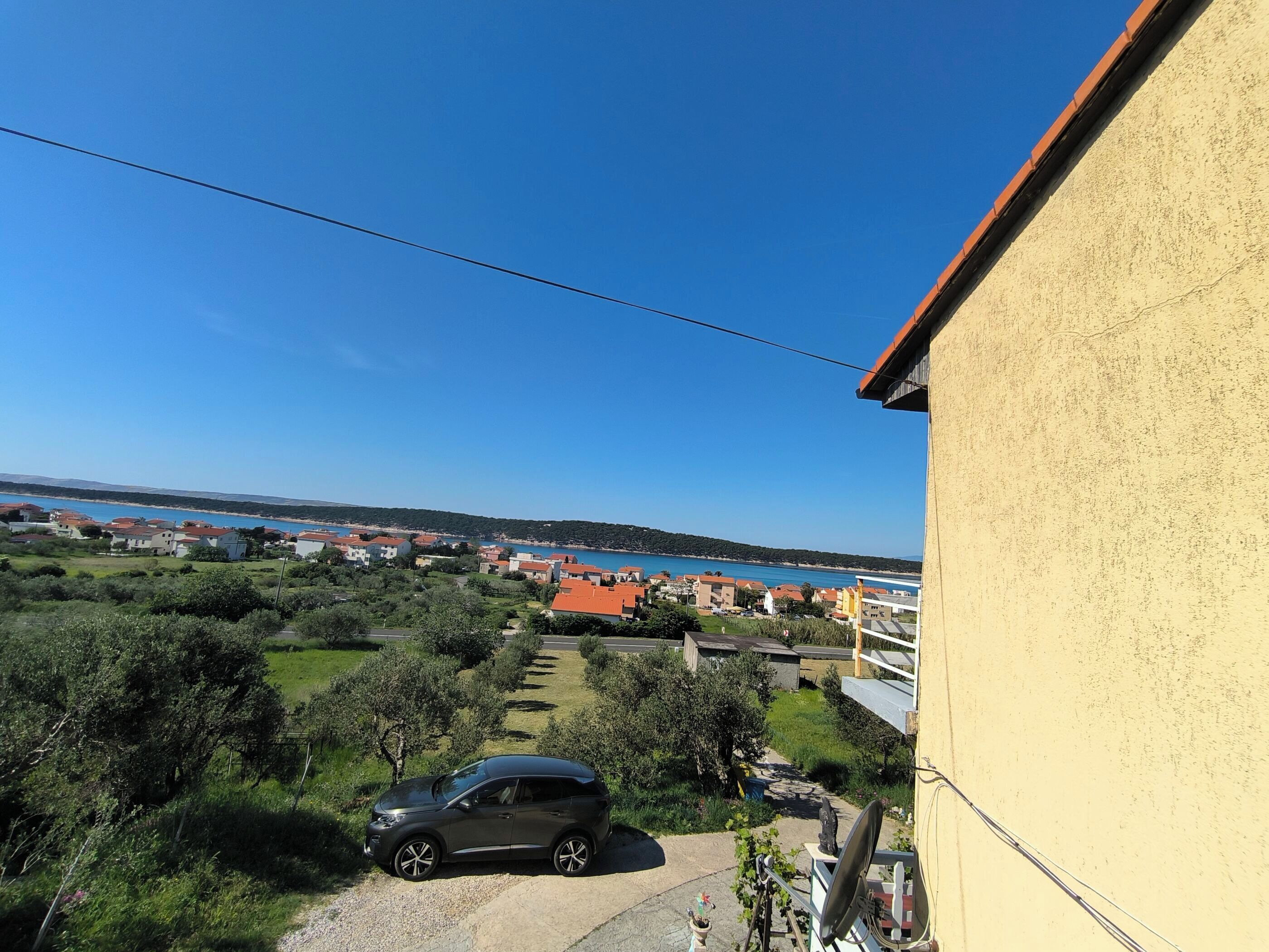 Un quartier résidentiel avec une voiture garée dans une allée, un ciel bleu dégagé et une vue lointaine sur la côte.