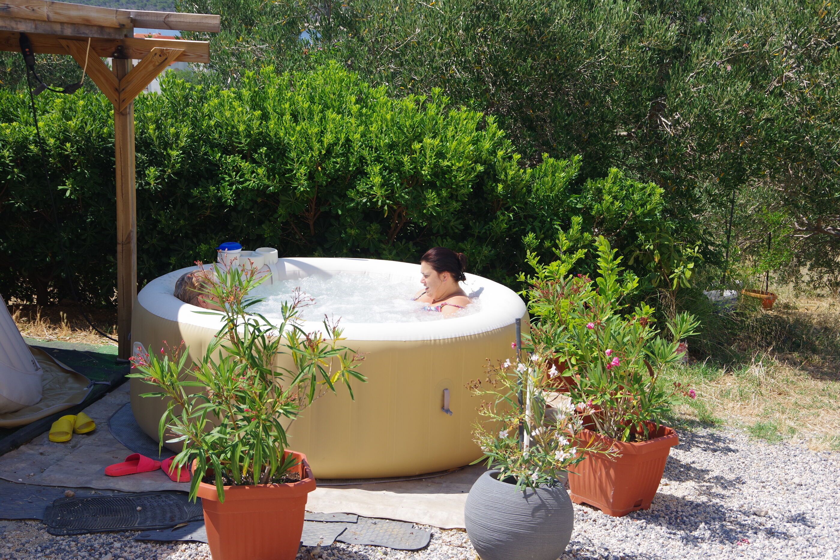 A hot tub in a garden with potted plants and a pergola.