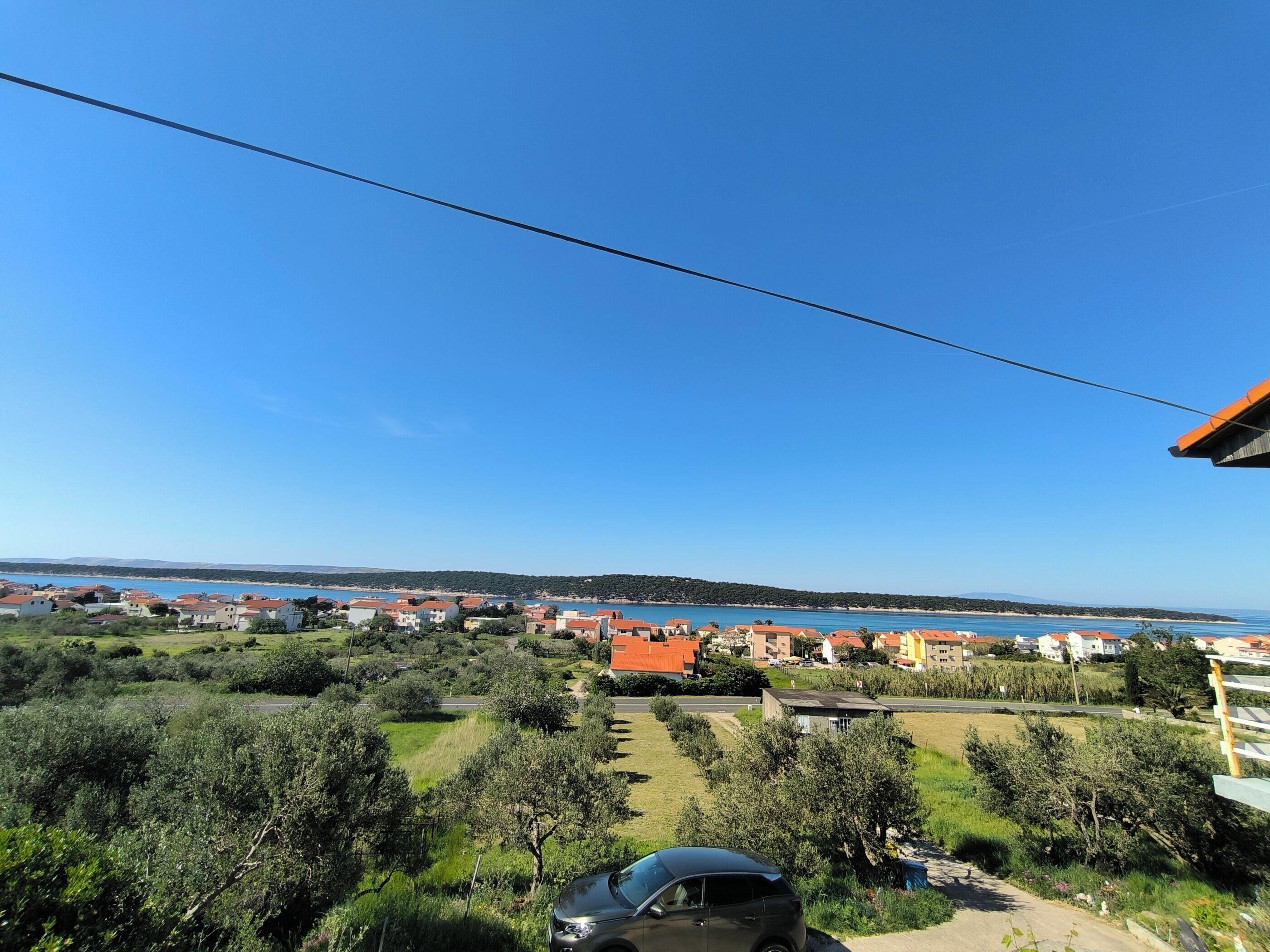 A coastal residential area with houses, a clear blue sky, and a car parked in the foreground.