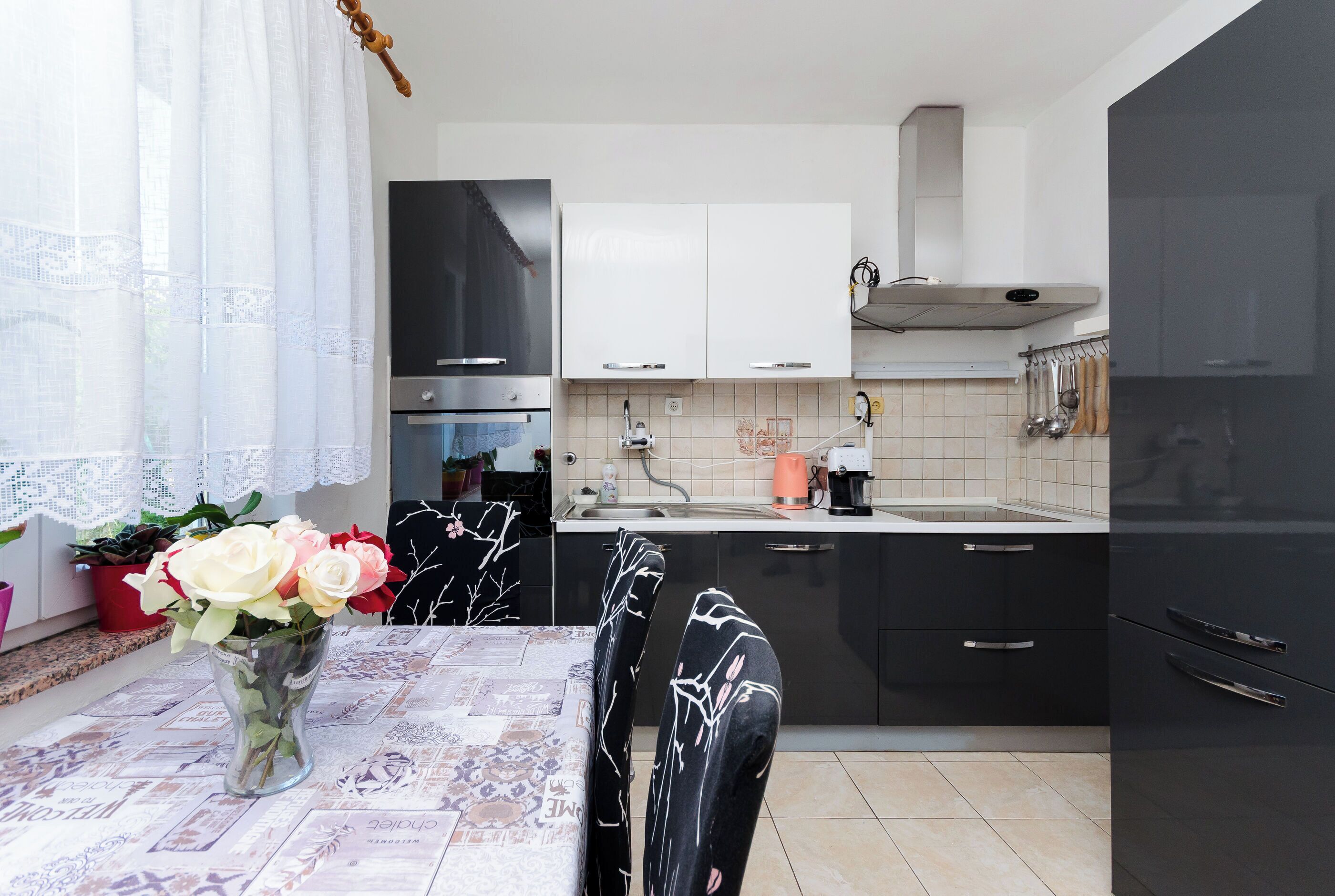 Una cocina moderna con armarios blancos y negros, una campana extractora de acero inoxidable y un comedor con una mesa para dos.