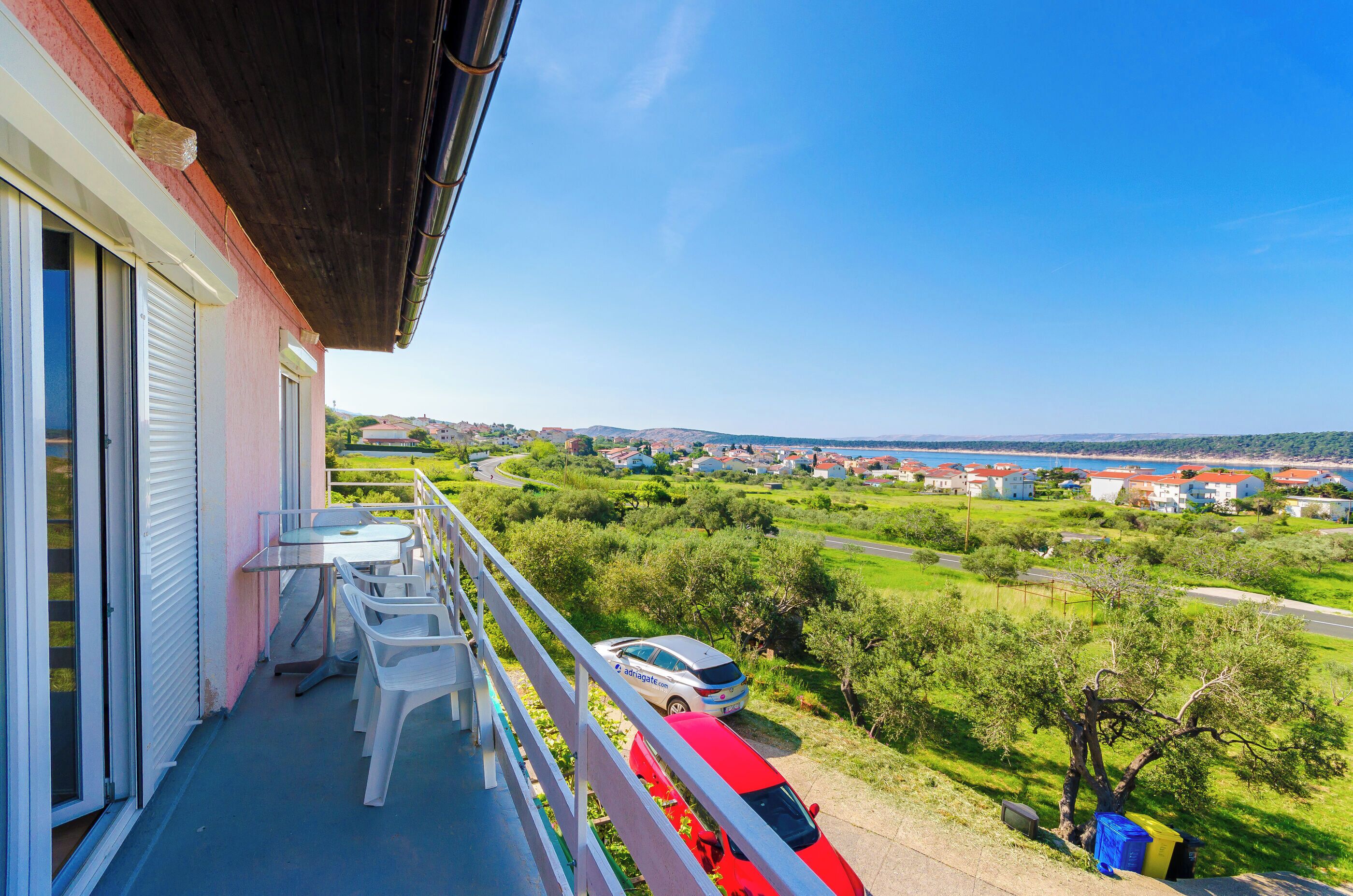 Varanda com mesa e cadeiras, com vista para uma área residencial com casas e uma rua.