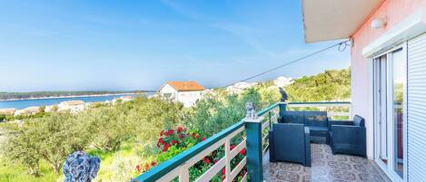 Un balcon aménagé avec du mobilier d’extérieur, un chien, et une vue sur la mer et la verdure.
