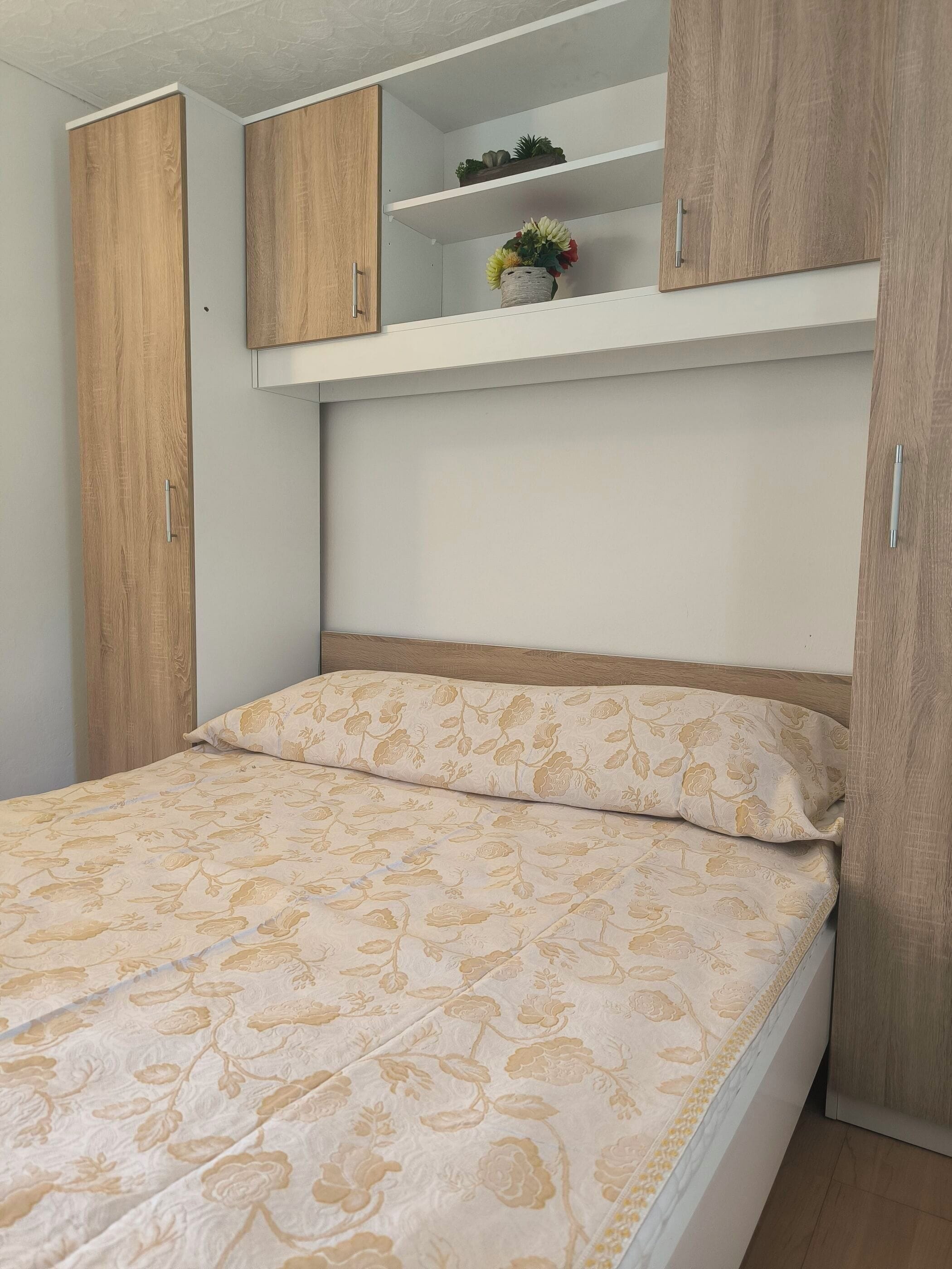 A bedroom with a bed, wooden wardrobe, and a shelf with decorative items.