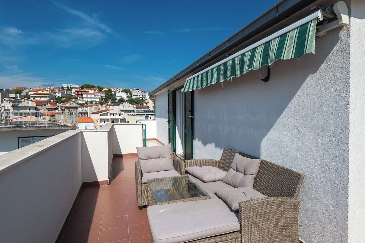 A balcony with wicker furniture, a view of a town, and a green-striped awning.