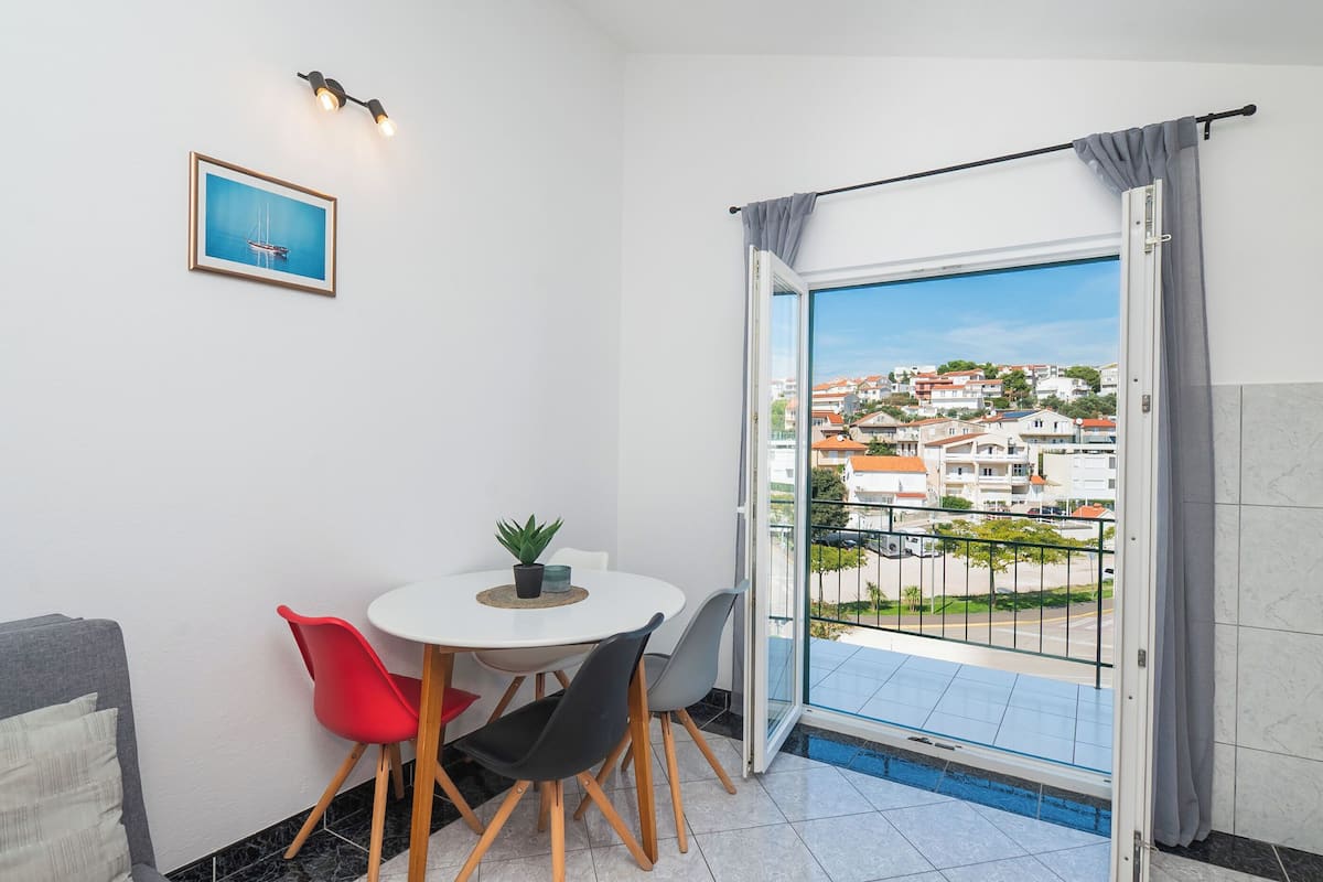A small balcony with a view of a residential area, a dining table with chairs, and a framed picture on the wall.