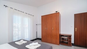 Ett hotellrum med en säng, en garderob, ett skrivbord med en stol och ett fönster med gardiner.