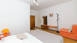 Ein Schlafzimmer mit einem Bett, einem orangefarbenen Sofa, einem Holzschrank, einem Schreibtisch mit Stuhl und einem Kleiderständer.
