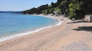 Ein Strand mit klarem, blauem Meer, sandigem Ufer und einem Gebäude mit Dach auf der rechten Seite.