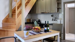 A kitchen with wooden cabinets, a dining table with a fruit basket and wine bottles, and a staircase.