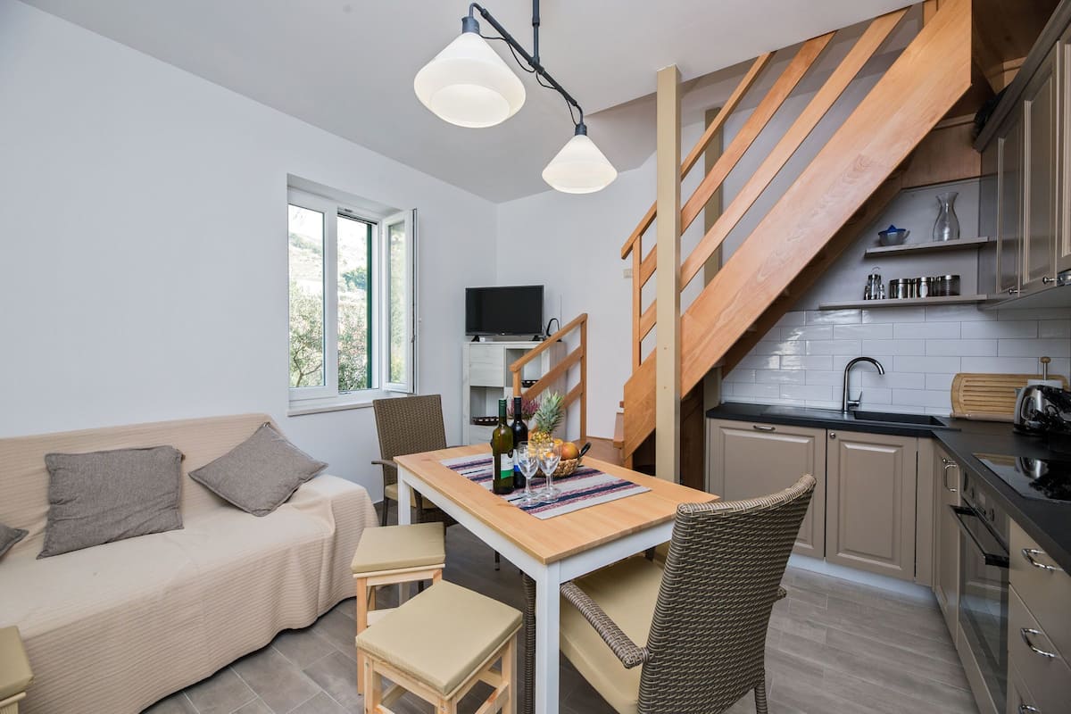 A compact living space with a sofa, dining table, chairs, a kitchen area, and a staircase.
