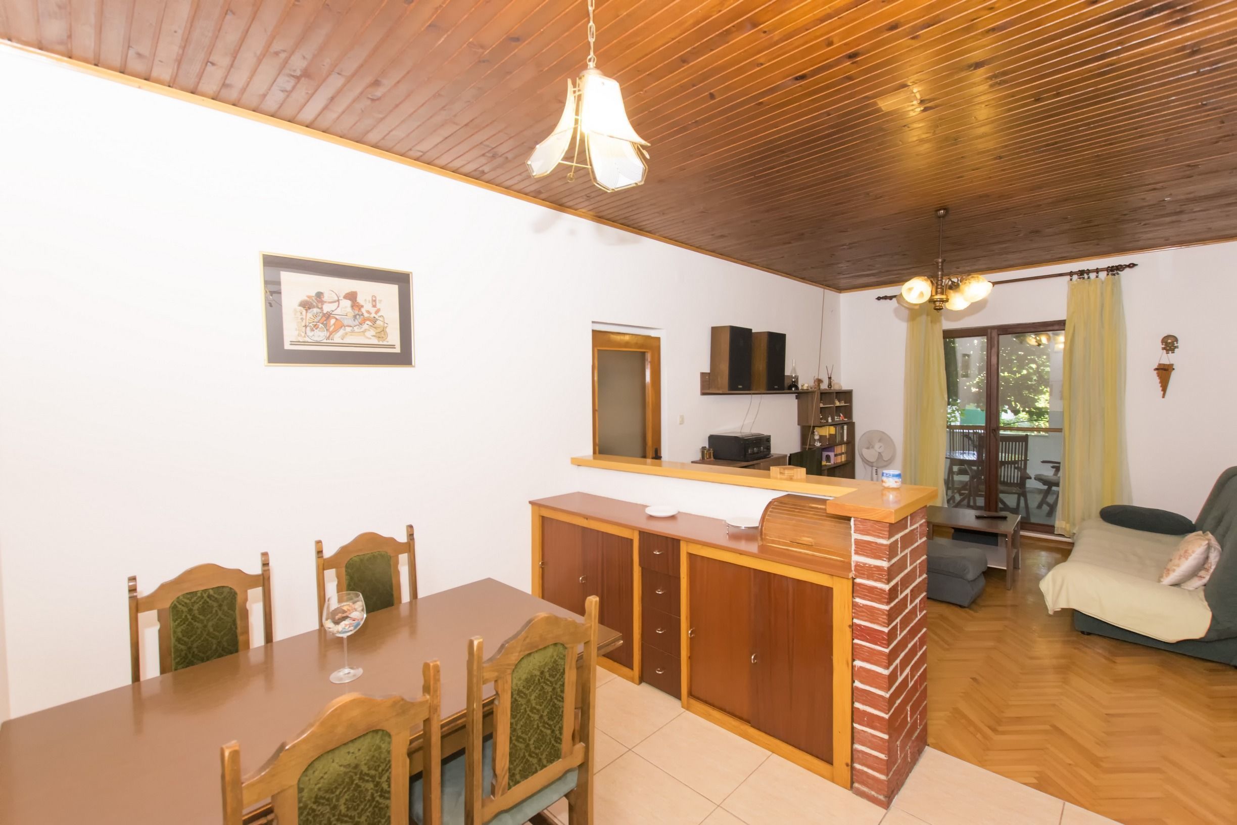 A dining area with a wooden table and chairs, a kitchen counter with a sink, and a living area with a sofa and a window.
