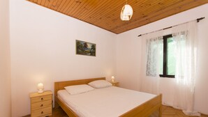 Un dormitorio con cama de madera, mesitas de noche, una mesilla auxiliar, un cuadro en la pared y una ventana con cortinas traslúcidas.