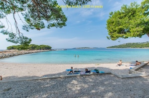 A beach with clear turquoise water, people sunbathing, and a rocky shoreline. - Apartment Alda (Murter)