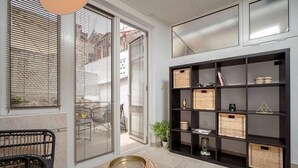 Ett modernt vardagsrum med en svart bokhylla, en korg av rotting och ett soffbord i glas.